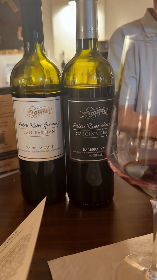 A glass of Barbera in front of the San Bastian and Cascina Perno bottles